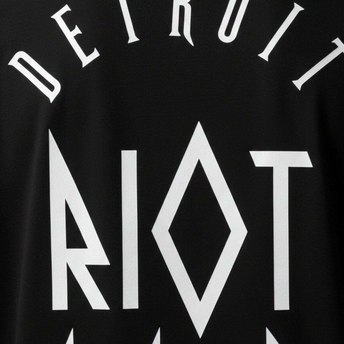Macro view of the Detroit Riot Club brand name going down the back of the shirt, graphic letter design on the back of a premium cotton streetwear garment, showcasing high-density print quality and intricate surrealist artwork.
