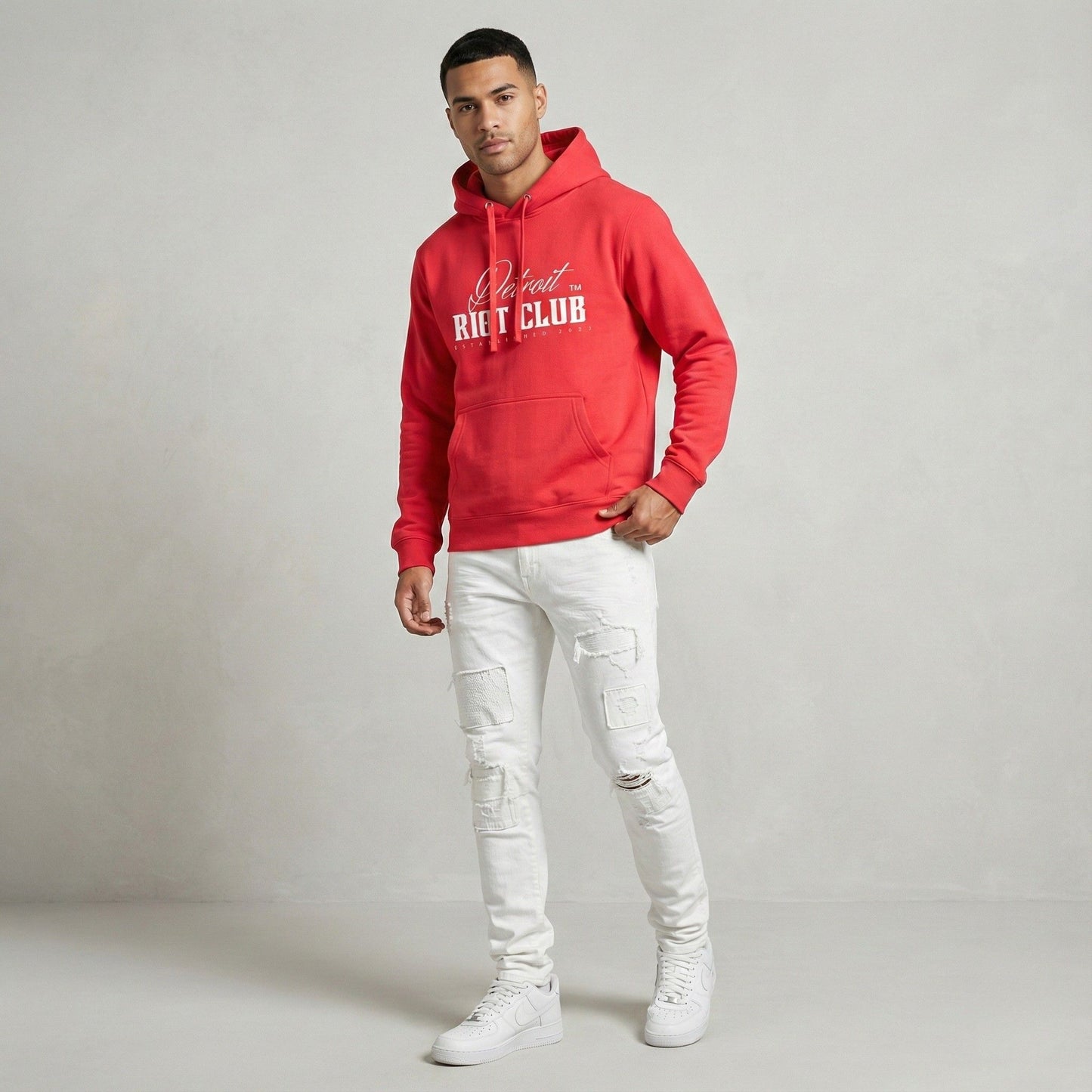 Person wearing a red hoodie with text and white pants on a gray background